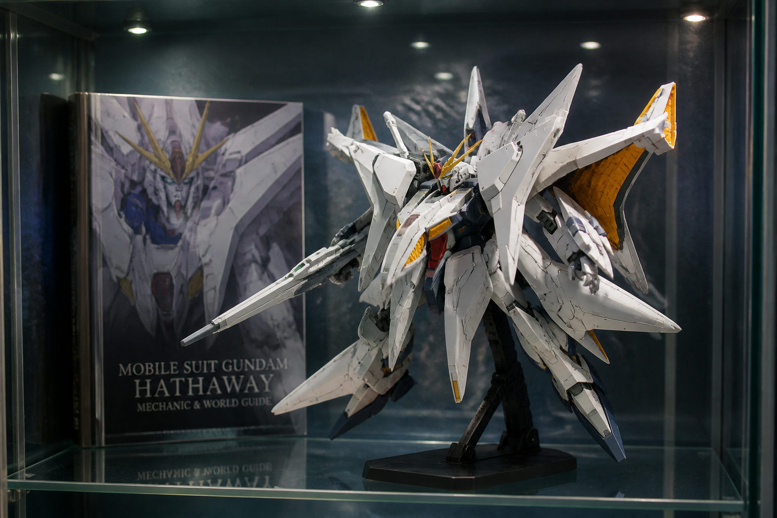 完成したガンプラがディスプレイケースの中に飾られ、背景に公式ガイドブックが置かれている様子